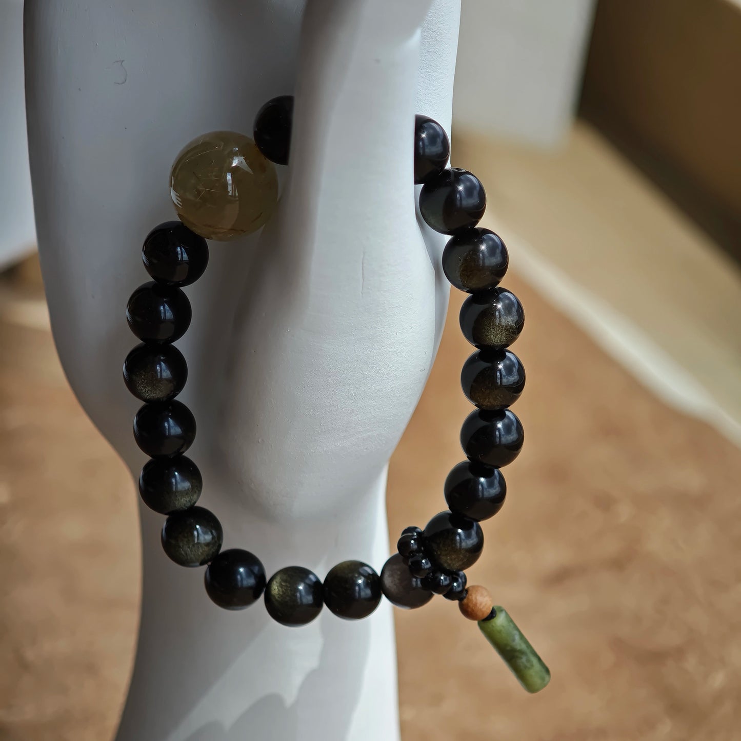 Crafted for defense, the strand balances gold-silver obsidian power with a rutile bead and a sandalwood-agate amulet touched by Eastern artistry.