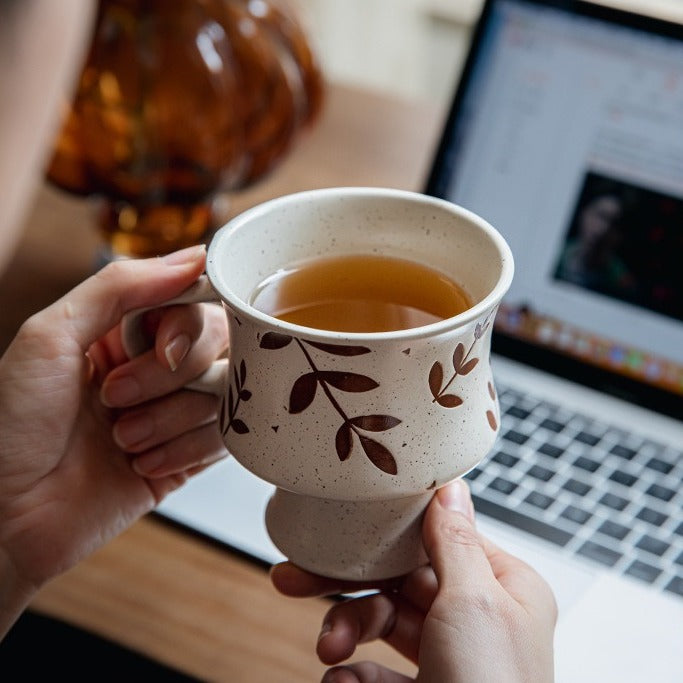 This is a 300ml ceramic goblet mug with hand-painted leaf or flower patterns and a matte sesame-speckled glaze design. With mouth diameter of 9.7, bottom diameter of 6.7cm and height of 10.5cm, this mug is ideal for coffee, milk, water, or oatmeal during slow mornings or quiet afternoons.