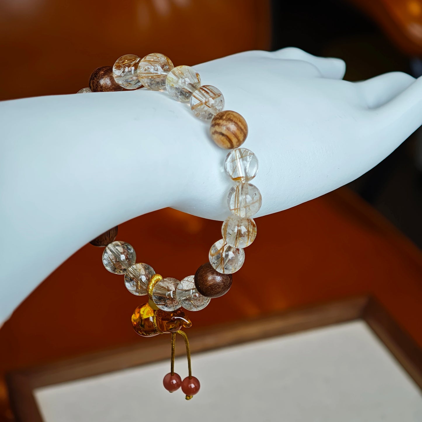 Golden-red needles flash against dark wood grain, while a carved amber gourd blossoms like a lucky lotus at the clasp.