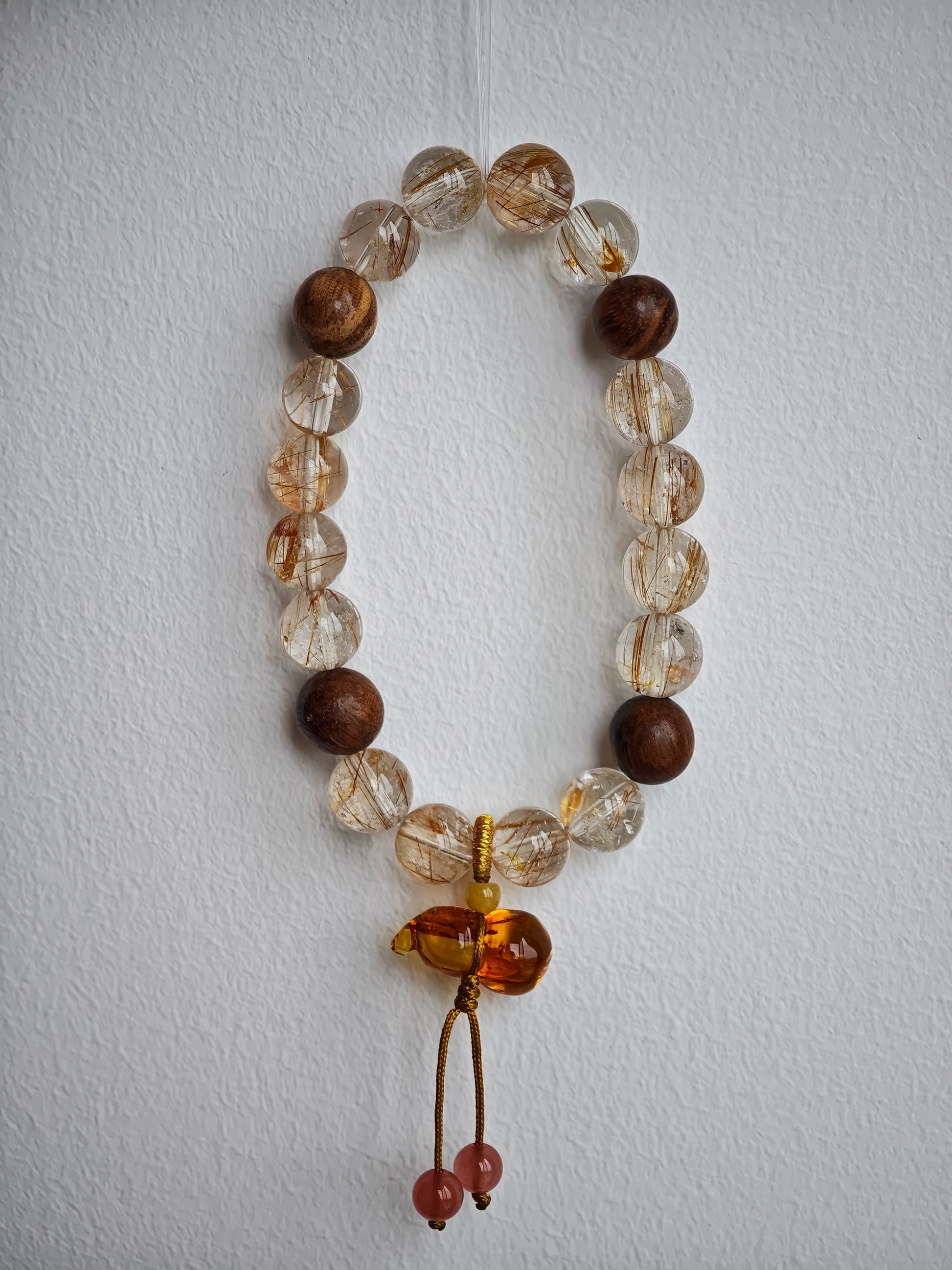 The bracelet braids lightning (copper rutile) with incense (agarwood) and ties the knot under a flowery lucky gourd.