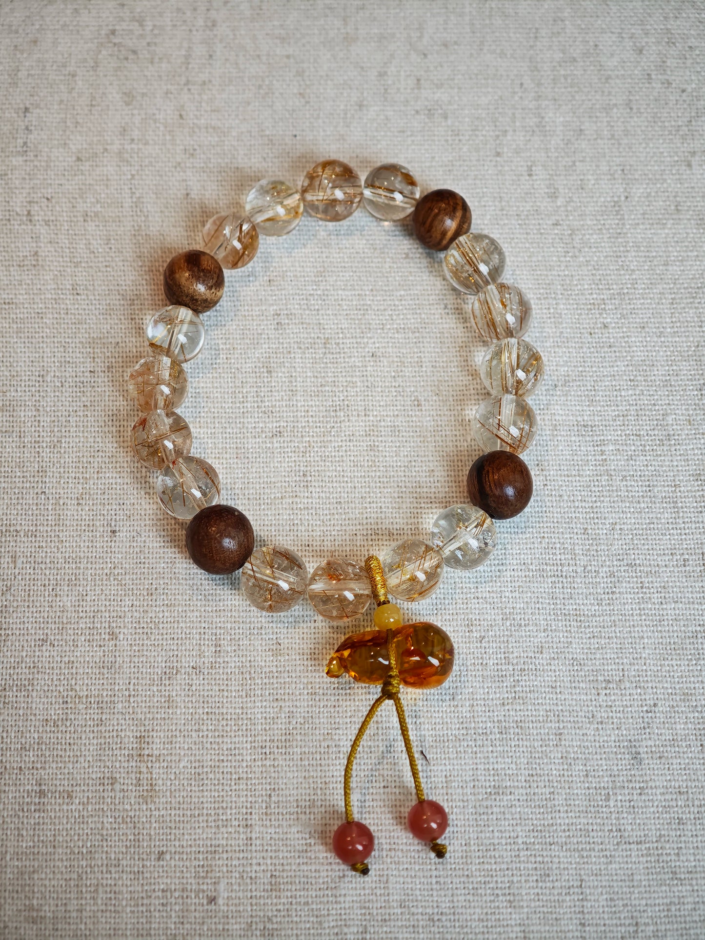 This crystal bracelet unites copper-rutilated quartz with aromatic agarwood beads, finished by a Nanhong-carved flower-amber gourd that symbolizes prosperity and protection.