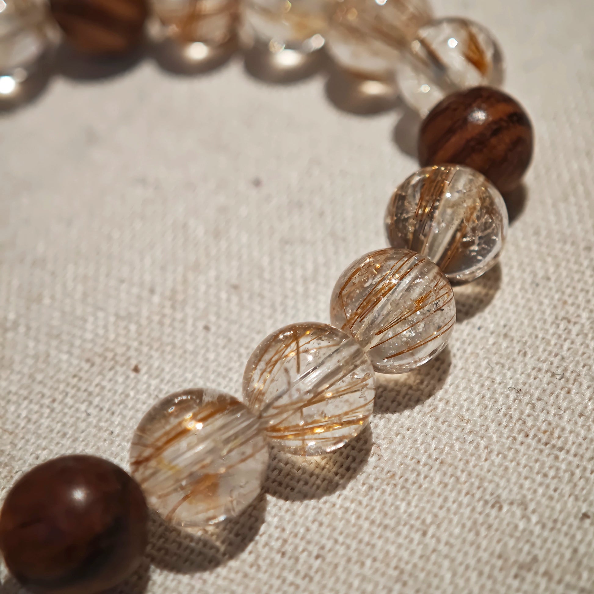 The bracelet pairs power crystals and sacred wood, then lets a flower-amber calabash dangle its twin seeds: prosper, protect.