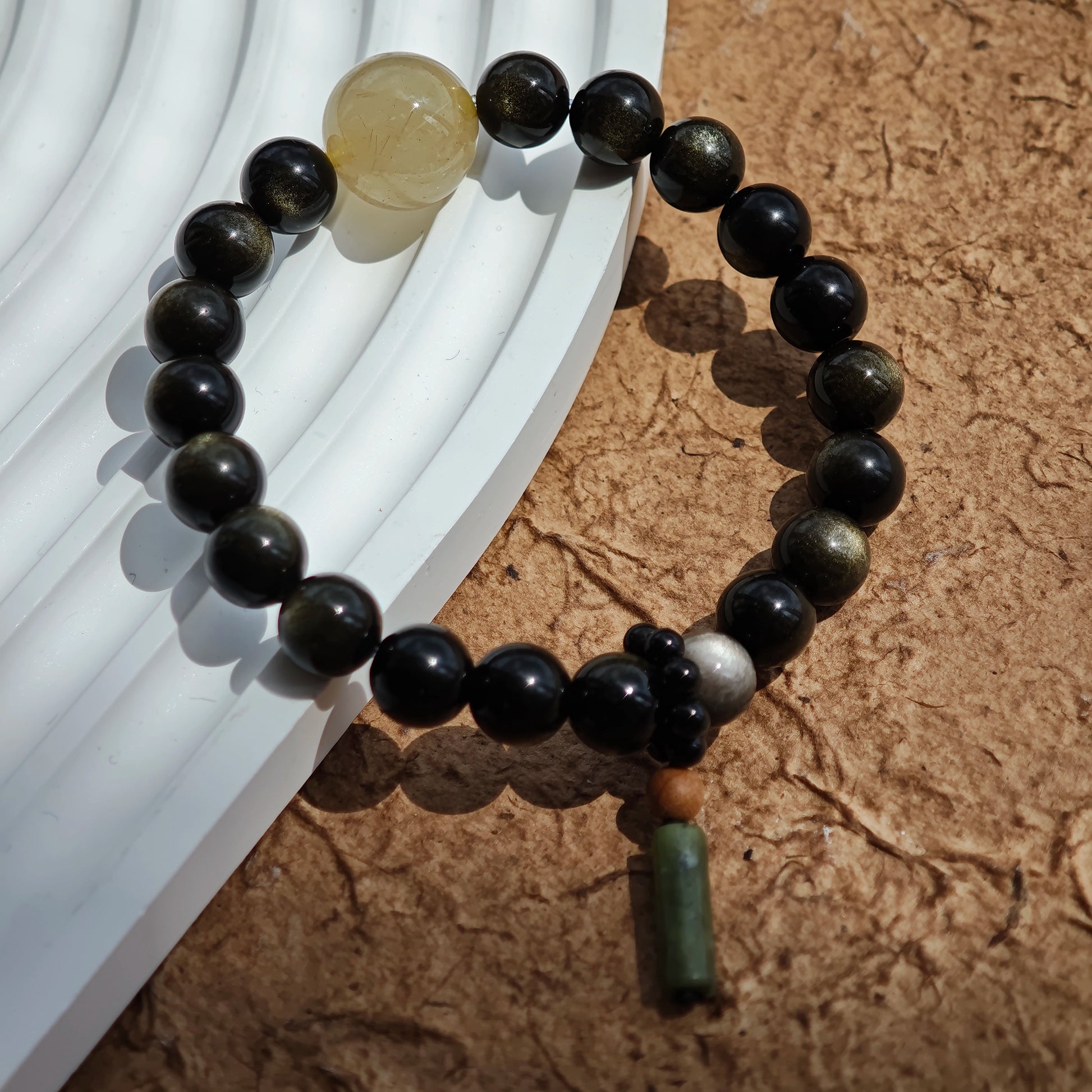 Clean lines of gold- and silver-sheen obsidian cradle a rutile bead and a sandalwood-black agate charm.