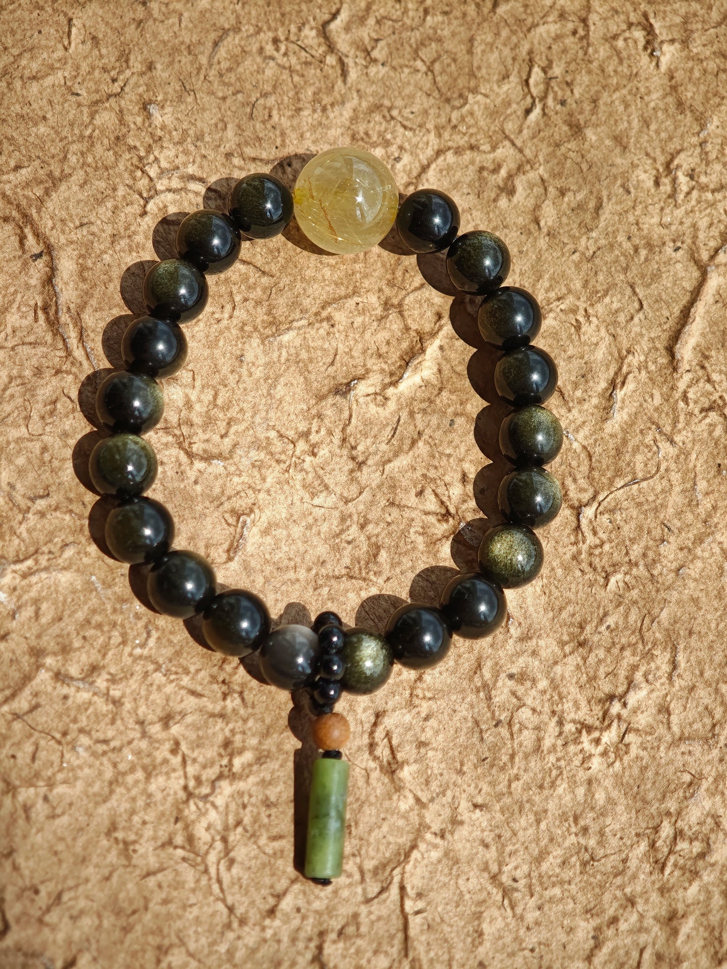 Radiant gold- and silver-obsidian orbs, a single rutile bead, and a sandalwood-agate pendant meld into a protective, culturally rich bracelet.