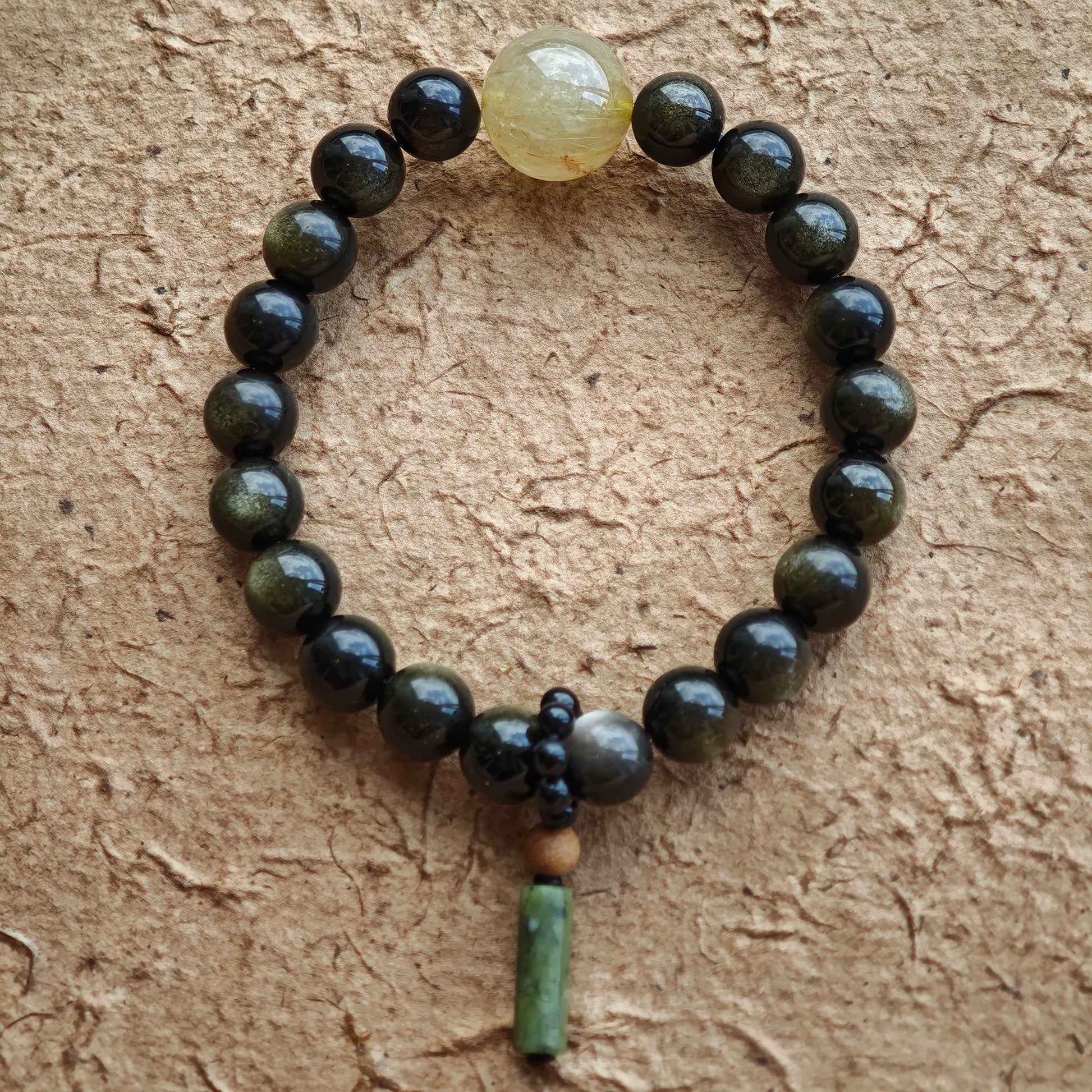 Eight-millimeter obsidian guardians circle the wrist, accented by rutilated quartz and a carved sandalwood-black agate token of China’s charm.