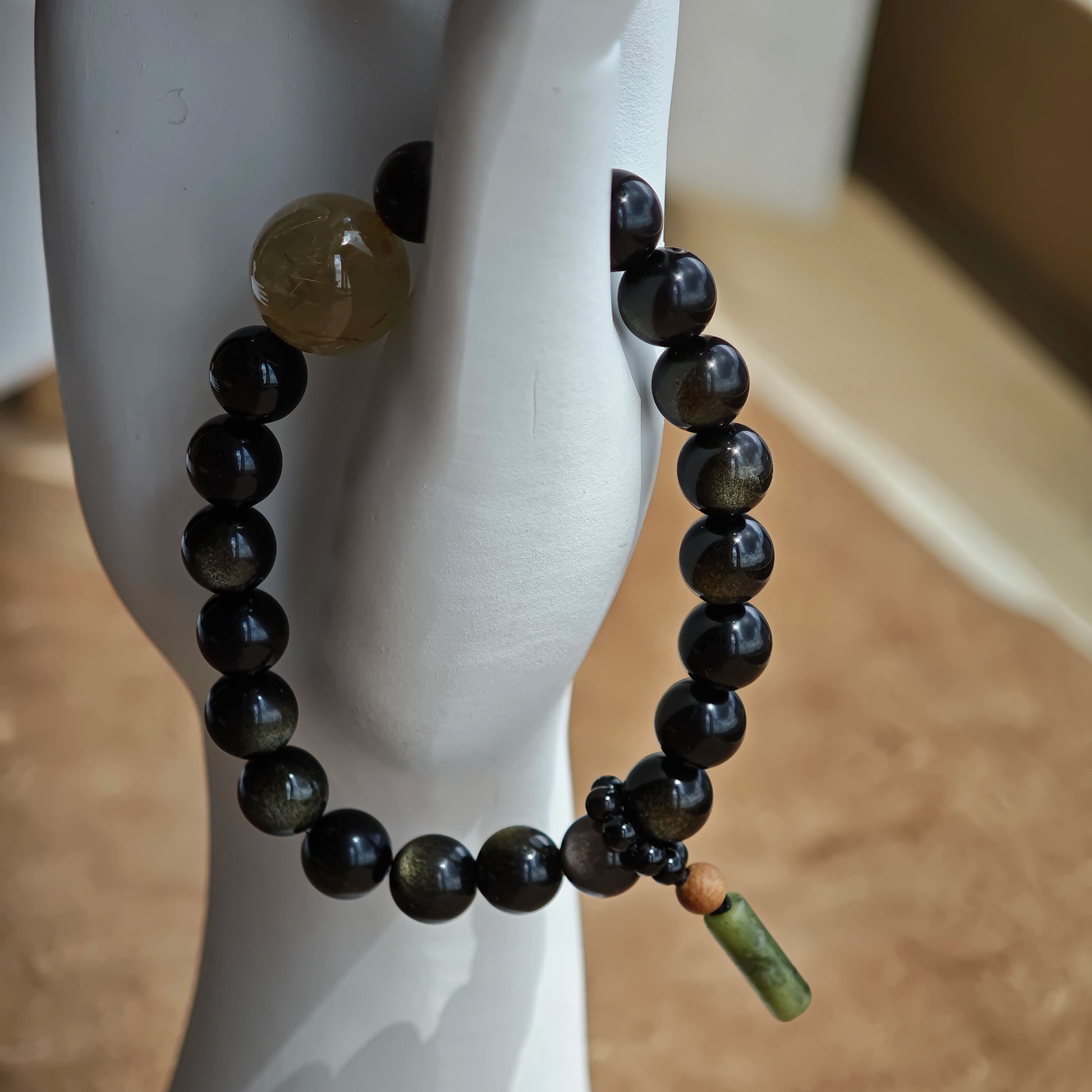 Crafted for defense, the strand balances gold-silver obsidian power with a rutile bead and a sandalwood-agate amulet touched by Eastern artistry.