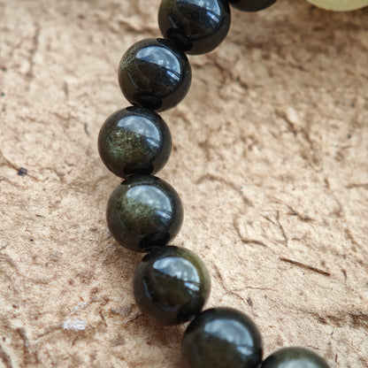 Gleaming gold-silver obsidian spheres, a rutile bead, and a carved sandalwood-agate drop craft quiet protection.