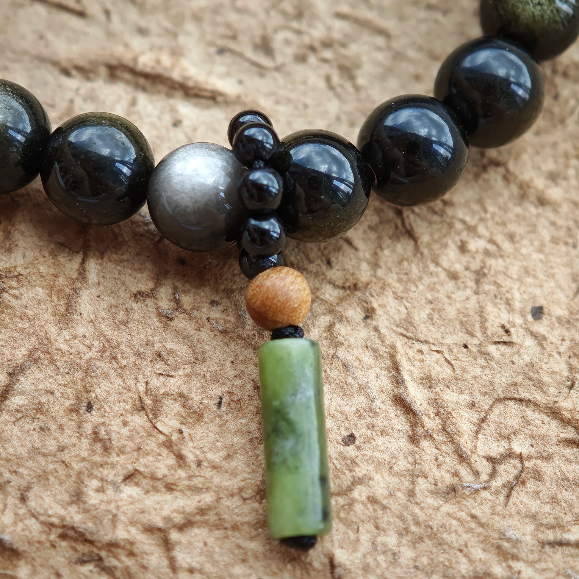 A dual-tone obsidian shield glows beside rutilated quartz and a sandalwood-black agate talisman.