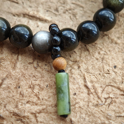 A dual-tone obsidian shield glows beside rutilated quartz and a sandalwood-black agate talisman.