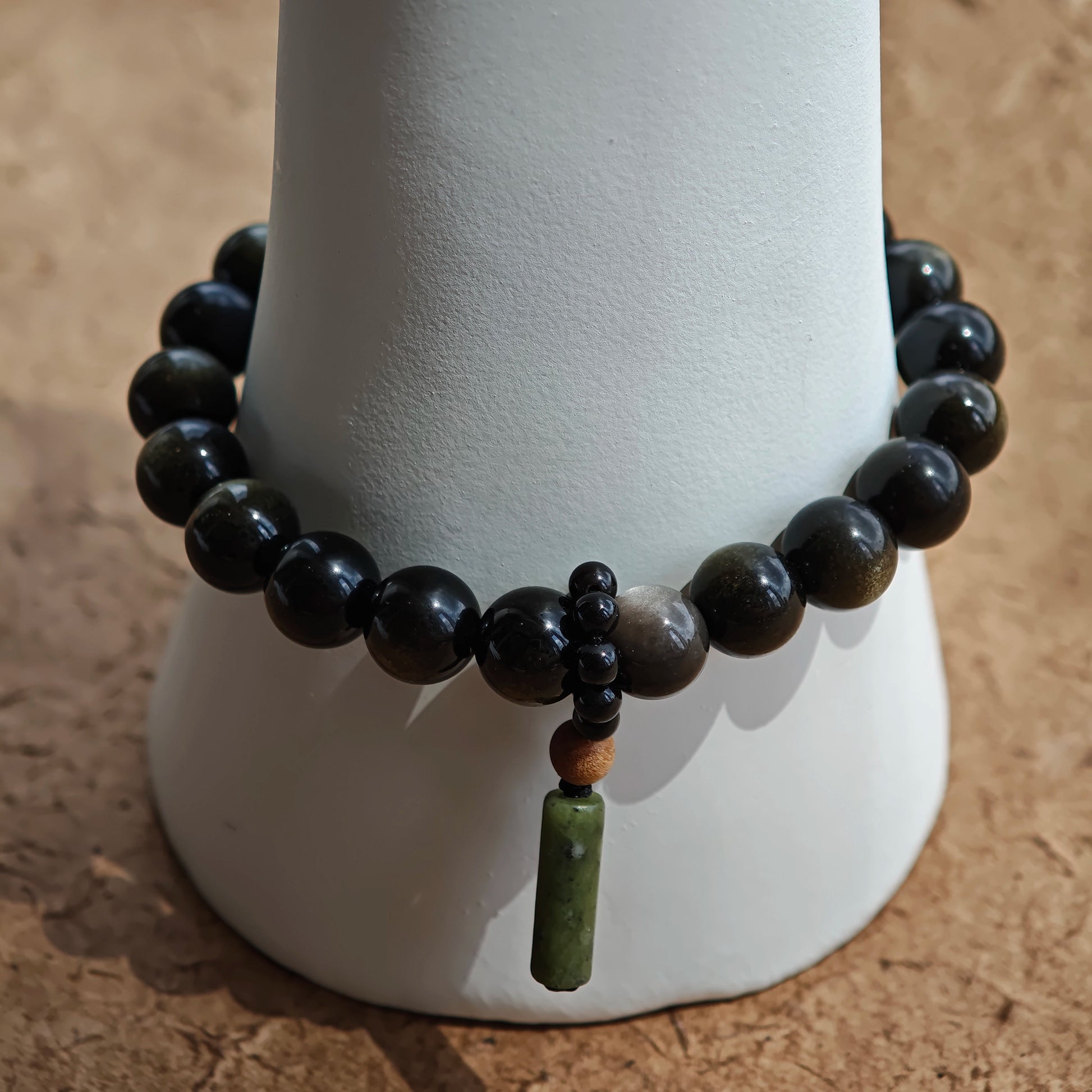 Eight-millimeter guardians in gold and silver obsidian frame a rutile bead and a sandalwood-agate amulet.