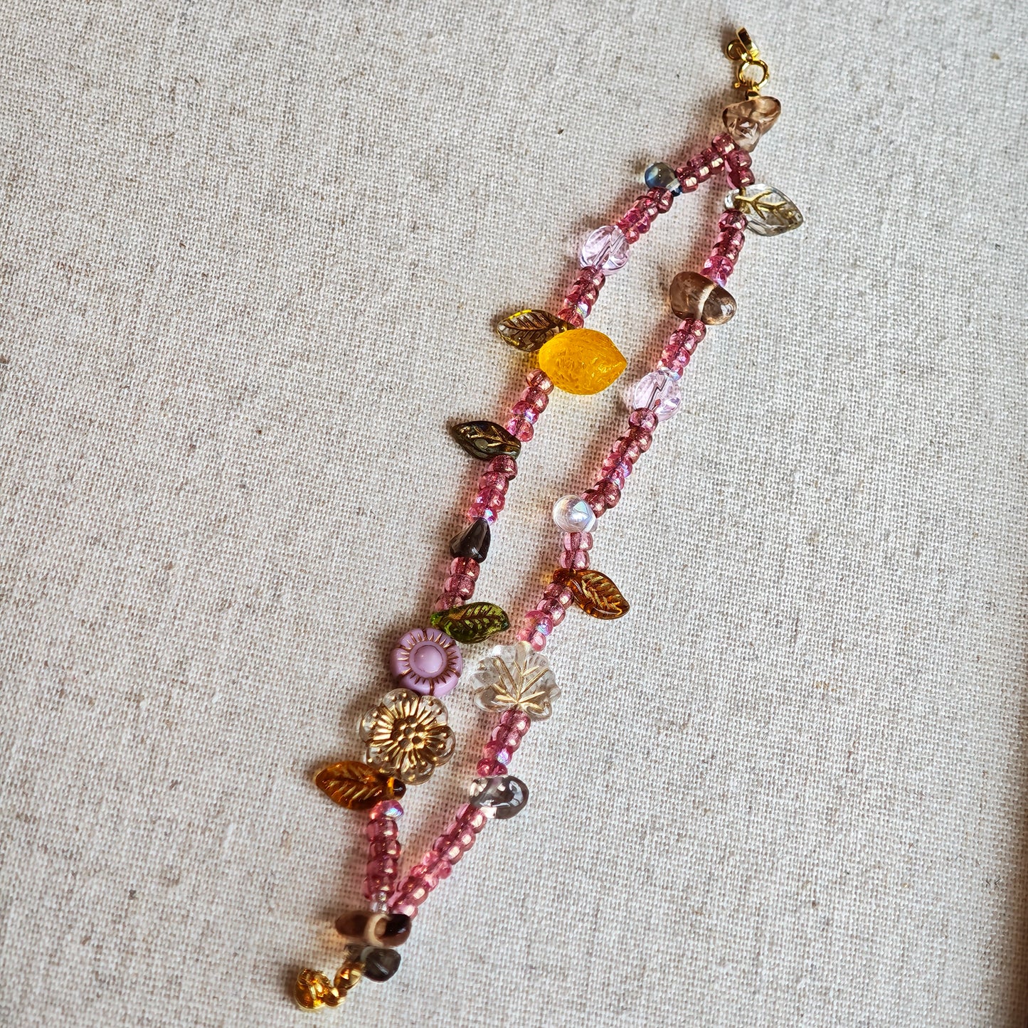 This is a pink czech beads bracelet, decorated with green leaves , yellow lemon, flowers and irregularly shape amber color beads.