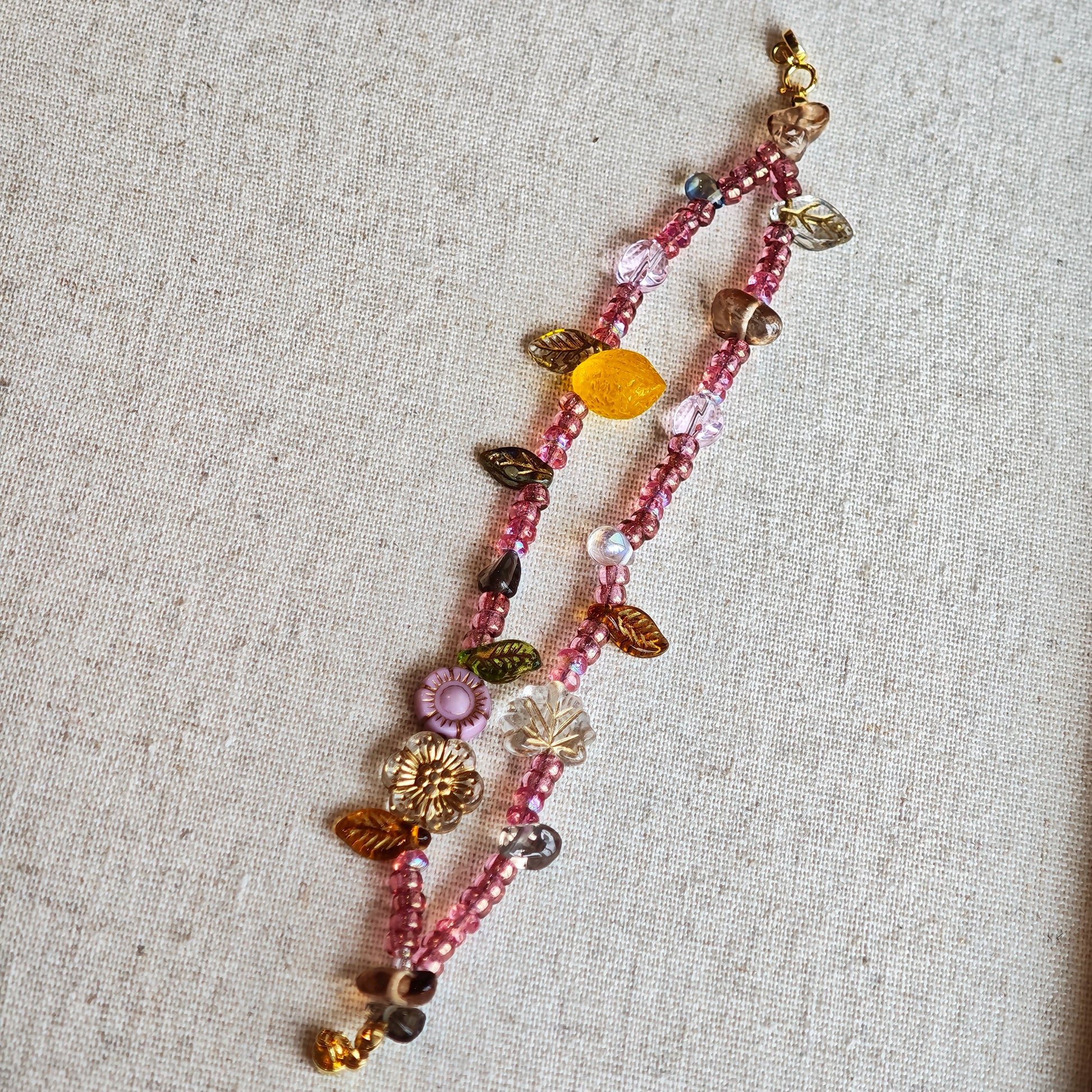 This is a pink czech beads bracelet, decorated with green leaves , yellow lemon, flowers and irregularly shape amber color beads.