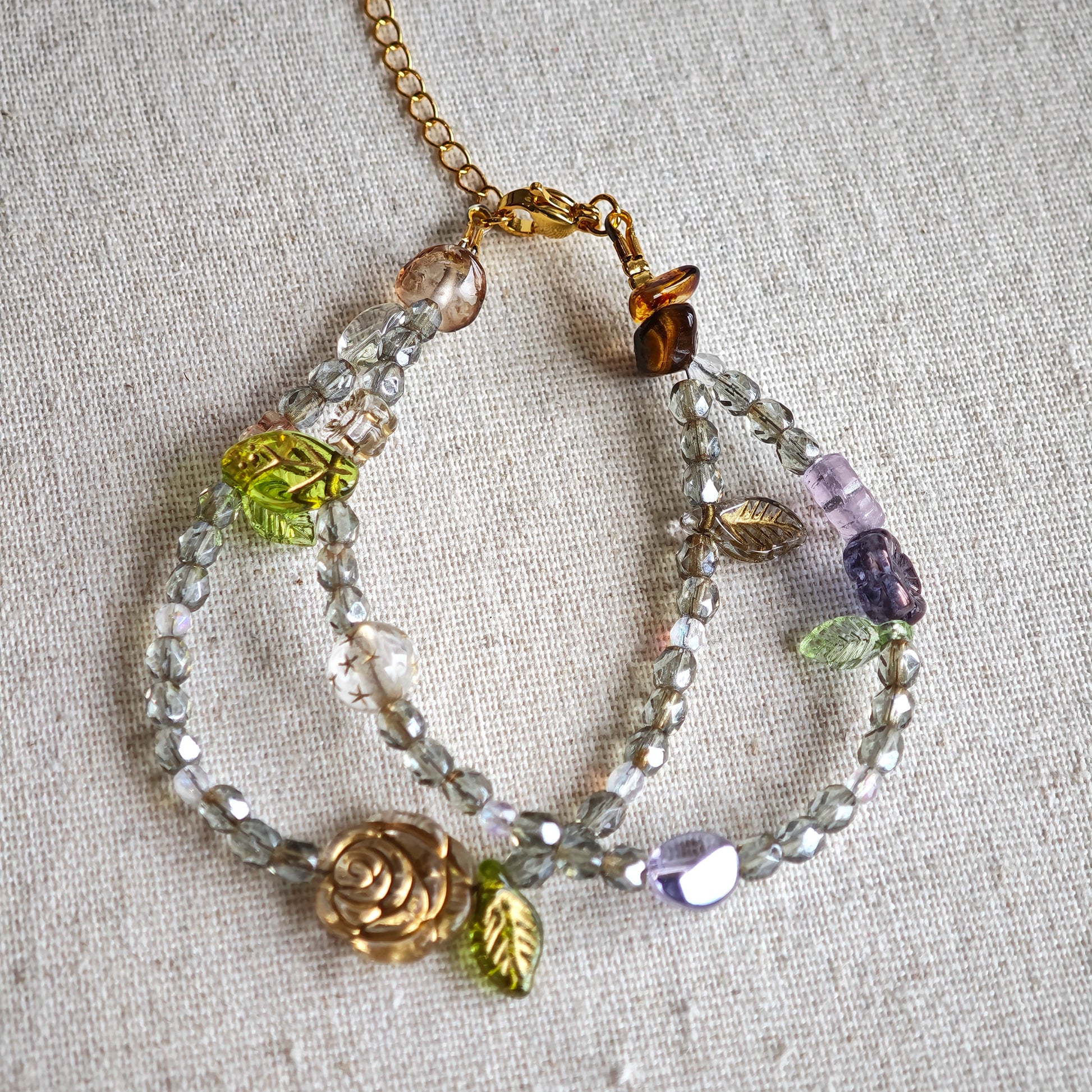 This is a grey czech beads bracelet, decorated with green leaves , bronze and purple flowers, and irregularly shape amber color spacer beads.