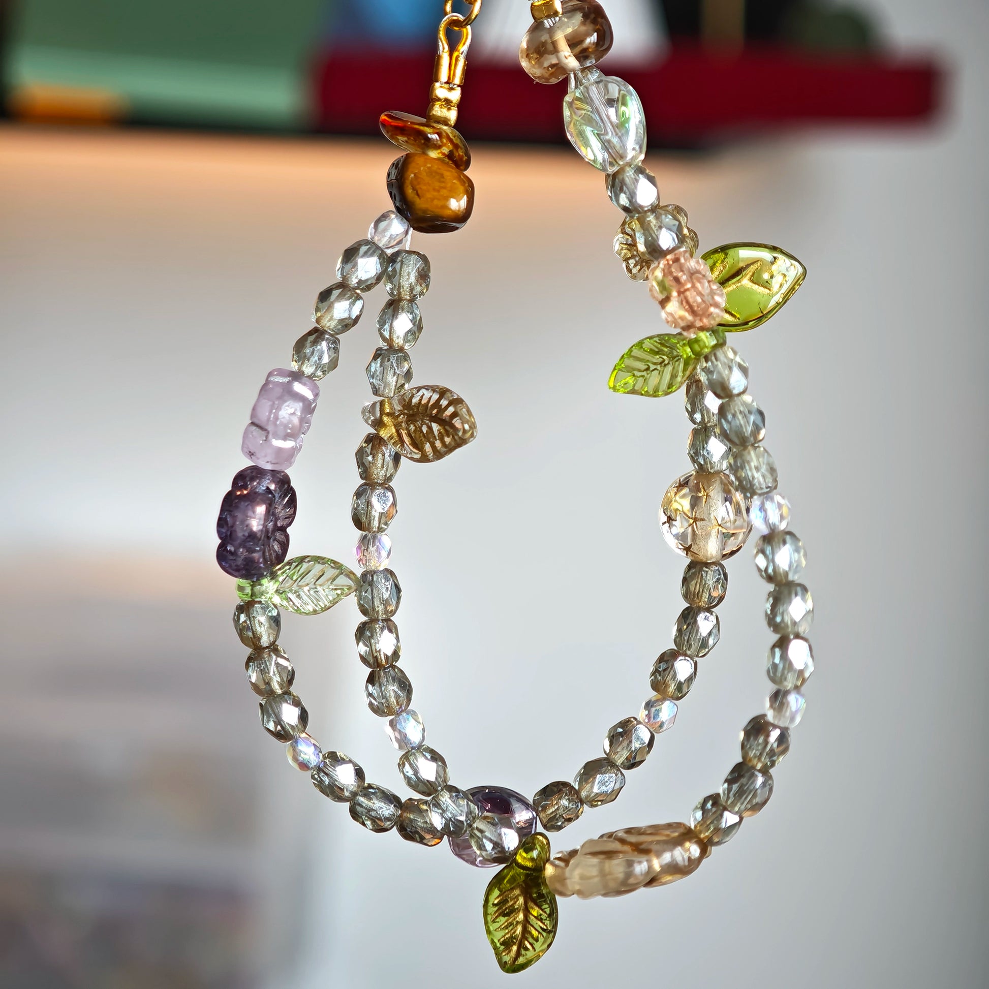 This is a grey czech beads bracelet, decorated with green leaves , bronze and purple flowers, and irregularly shape amber color spacer beads.