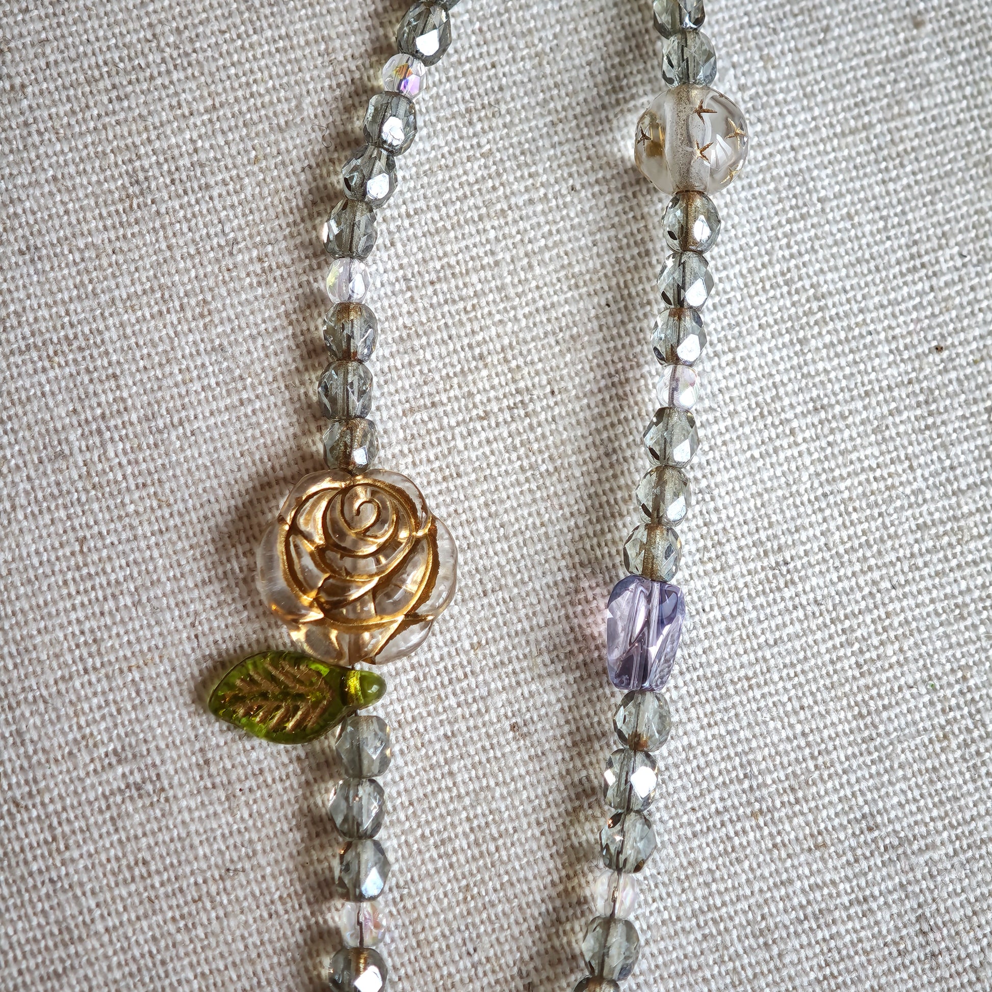 This is a grey czech beads bracelet, decorated with green leaves , bronze and purple flowers, and irregularly shape amber color spacer beads.