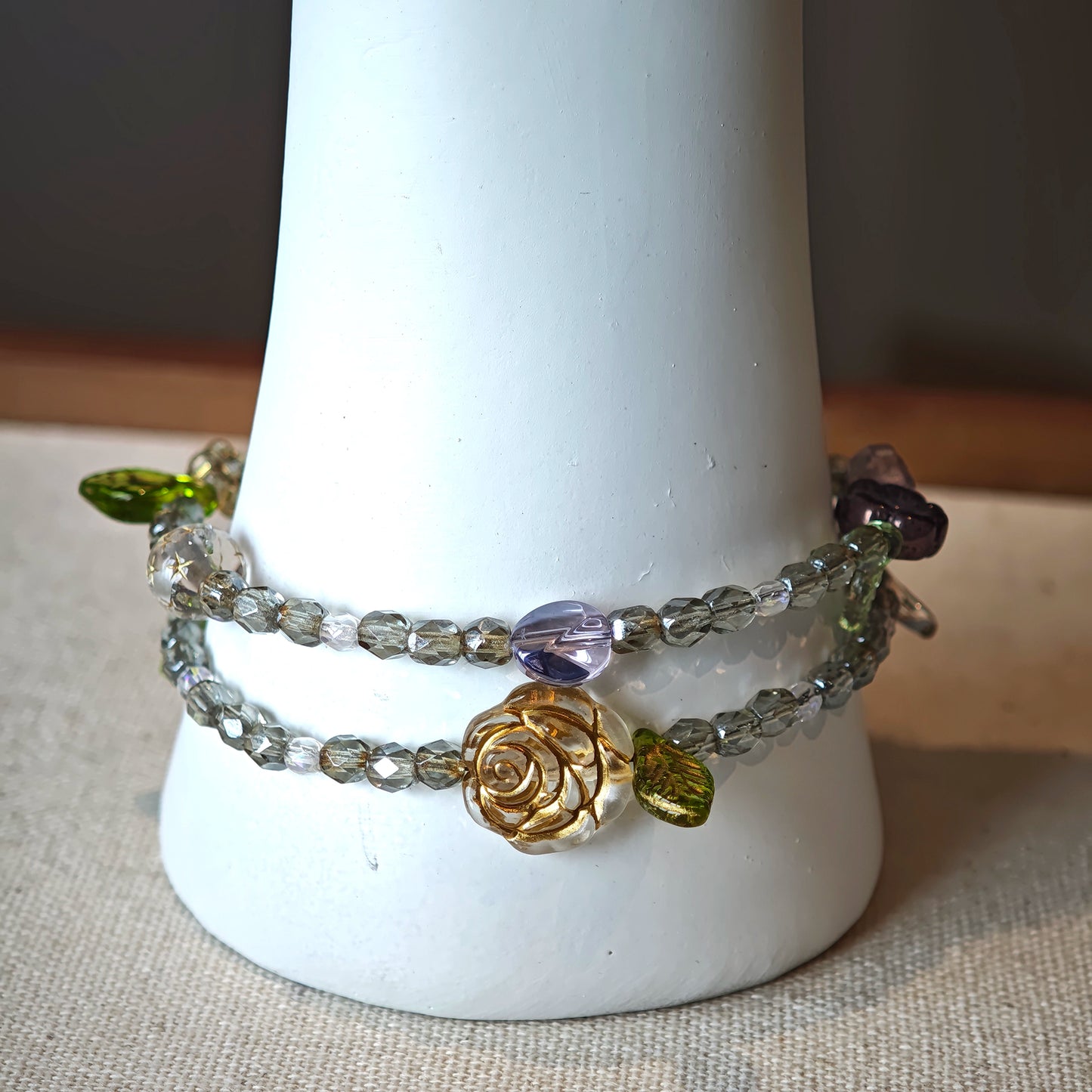 This is a grey czech beads bracelet, decorated with green leaves , bronze and purple flowers, and irregularly shape amber color spacer beads.