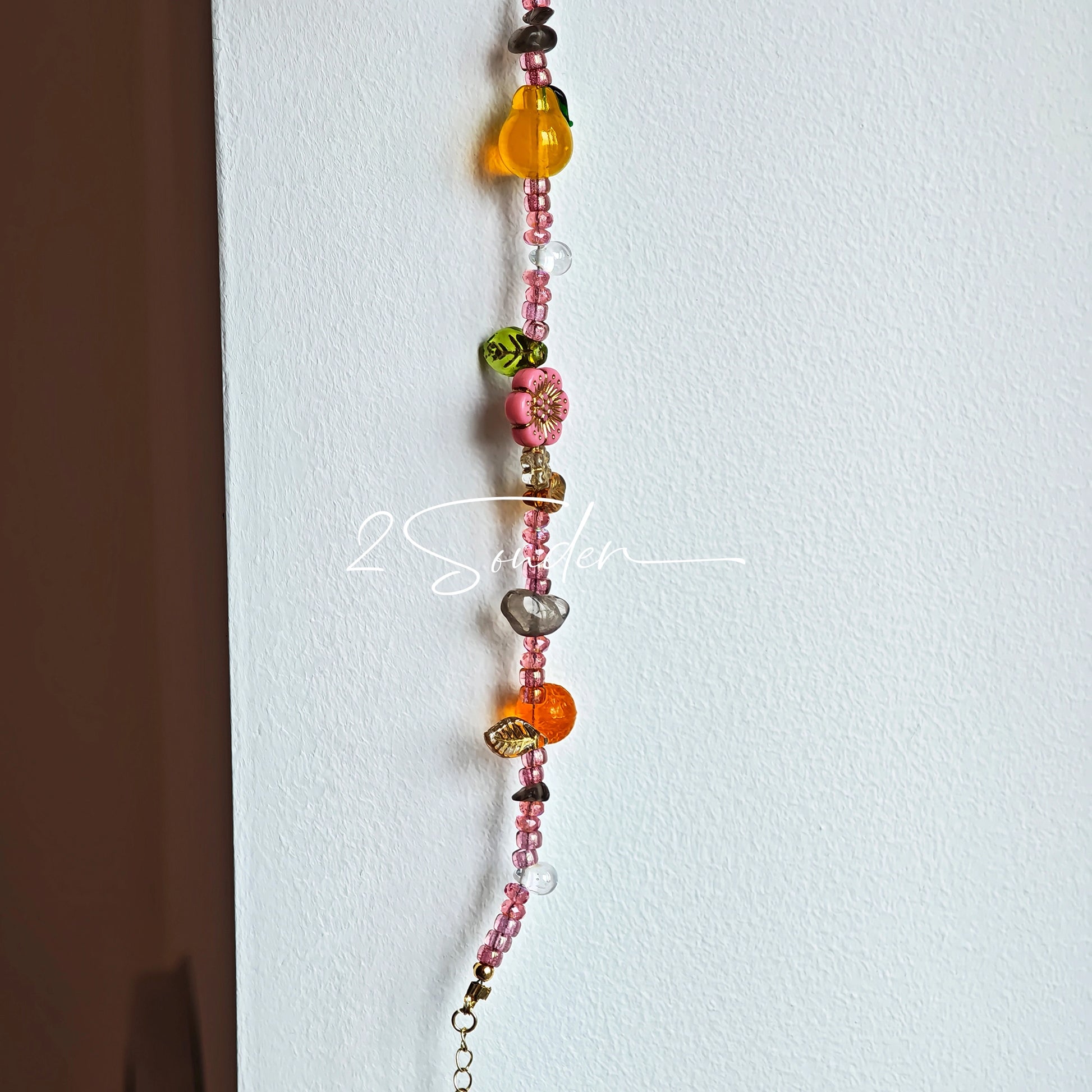This is a bracelet consist of glass beads. The main color of the bracelet is pink. It's also decorated with orange, yellow pear, grey flower, brown leaves and green leaves spacers.