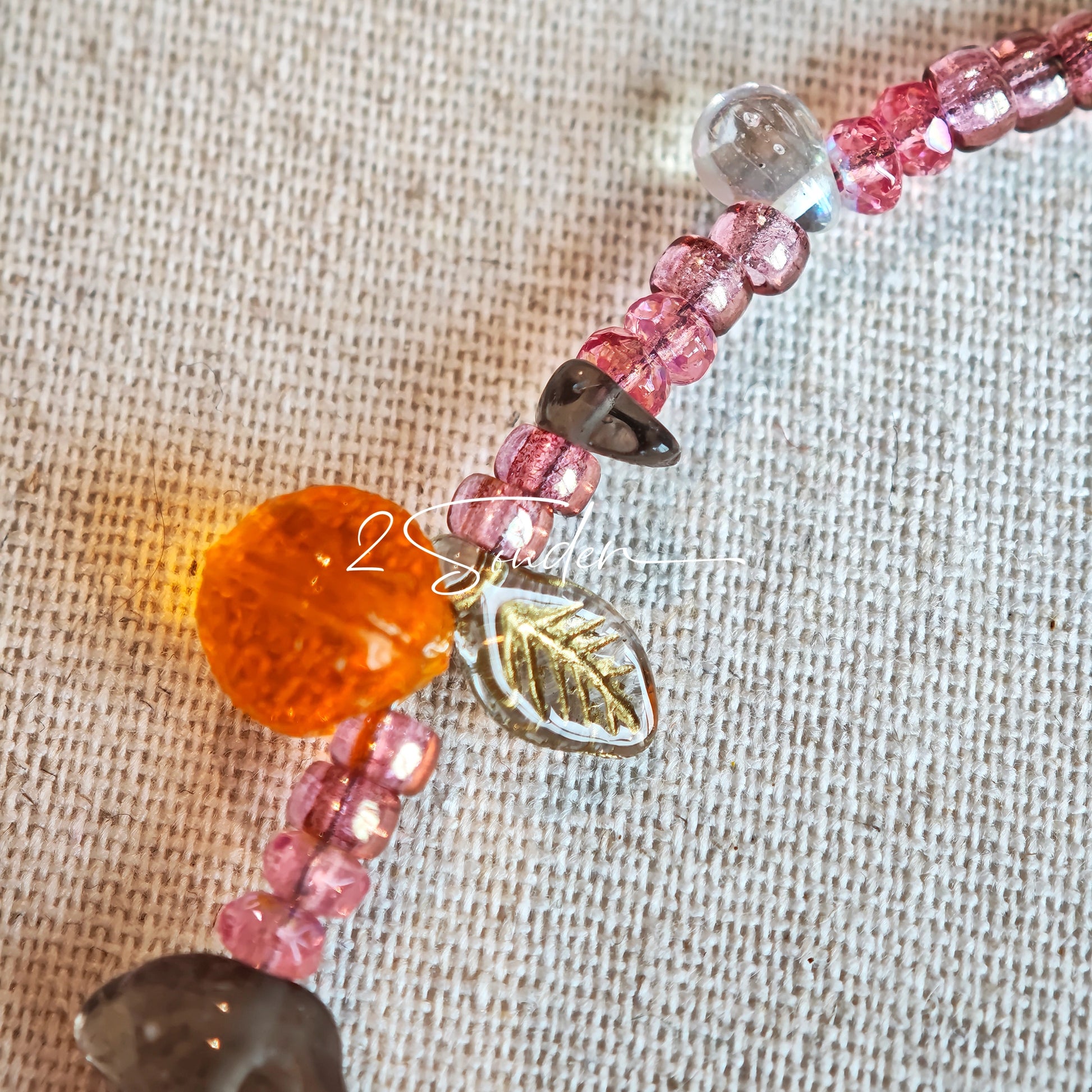This is a bracelet consist of glass beads. The main color of the bracelet is pink. It's also decorated with orange, yellow pear, grey flower, brown leaves and green leaves spacers.