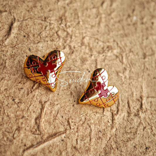 This is a pair of heart earrings with puzzle blocks pattern on the surface. The earrings feature a vibrant enamel center that mimics a beating heart flowing with love. The material of the earrings is sterling silver and enamel, and the color is vintage gold color