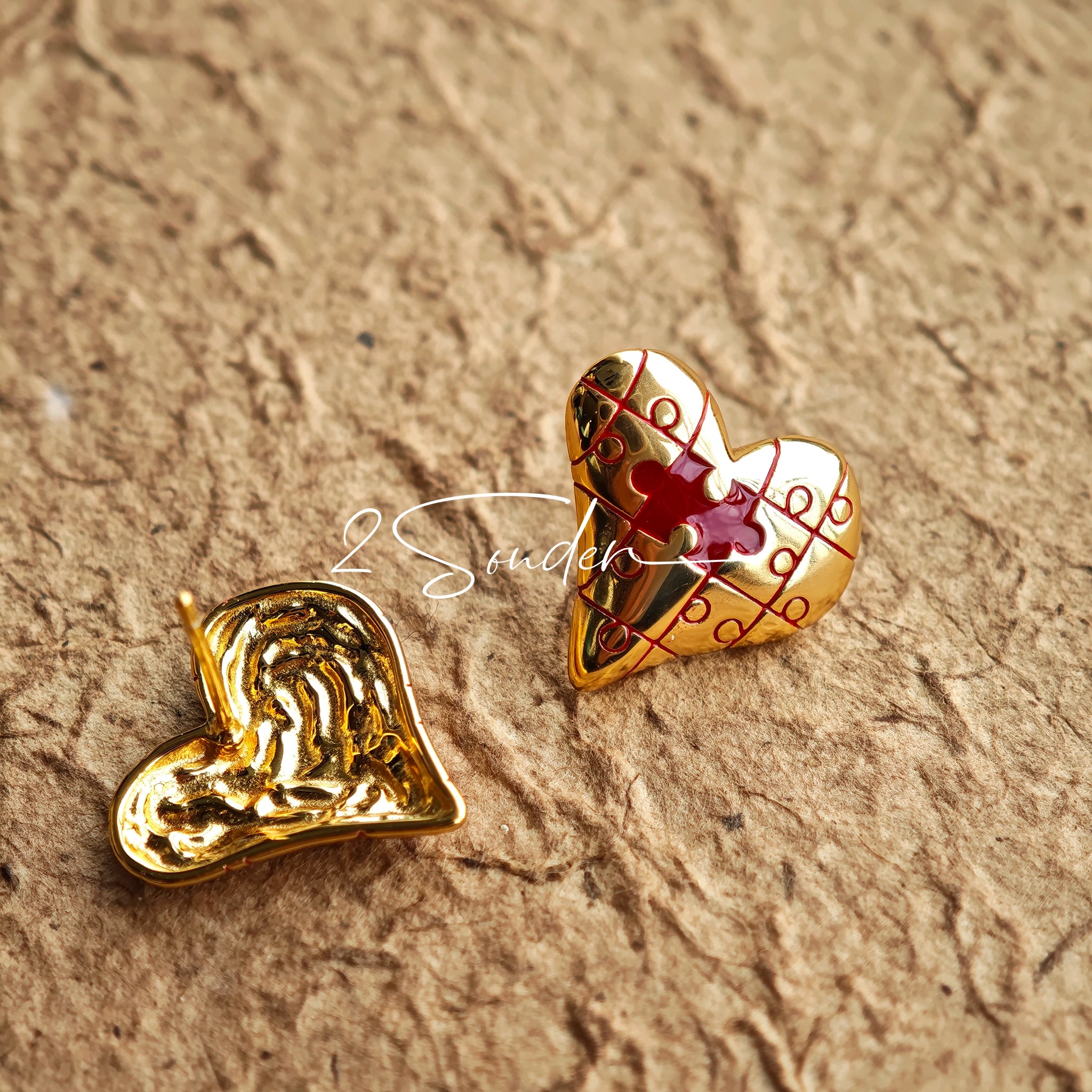 This is a pair of heart earrings with puzzle blocks pattern on the surface. The earrings feature a vibrant enamel center that mimics a beating heart flowing with love. The material of the earrings is sterling silver and enamel, and the color is vintage gold color