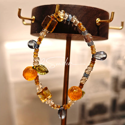This is a bracelet made of Czech beads, orange slice spacers, leaf spacers, blue teardrop accents and elastic cord. The beads’ crystal-clear translucency catches light like dewdrops—perfect for adding a luxe touch to everyday outfits.