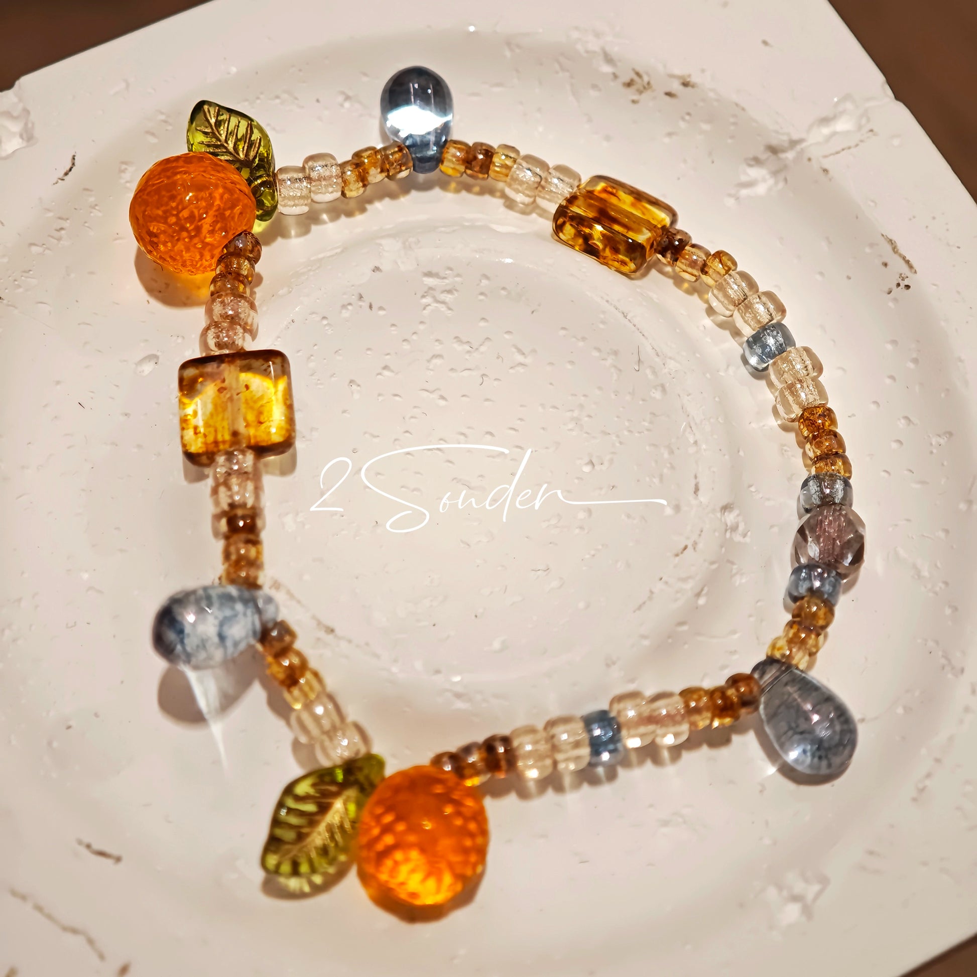 This is a bracelet made of Czech beads, orange slice spacers, leaf spacers, blue teardrop accents and elastic cord. The beads’ crystal-clear translucency catches light like dewdrops—perfect for adding a luxe touch to everyday outfits.