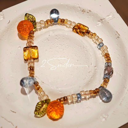 This is a bracelet made of Czech beads, orange slice spacers, leaf spacers, blue teardrop accents and elastic cord. The beads’ crystal-clear translucency catches light like dewdrops—perfect for adding a luxe touch to everyday outfits.