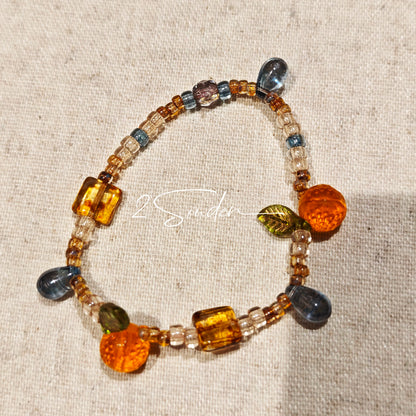 This is a bracelet made of Czech beads, orange slice spacers, leaf spacers, blue teardrop accents and elastic cord. The beads’ crystal-clear translucency catches light like dewdrops—perfect for adding a luxe touch to everyday outfits.
