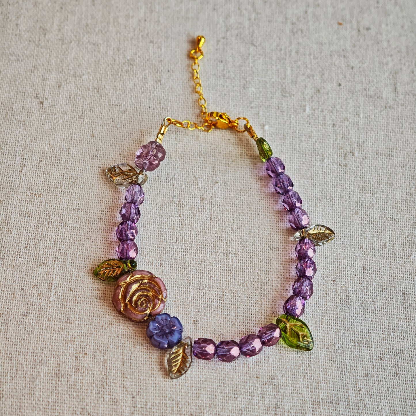 A purple hand-strung bracelet with luminous Czech glass beads & delicate botanical charms.