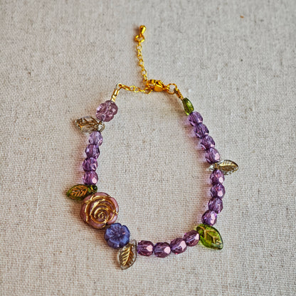 A purple hand-strung bracelet with luminous Czech glass beads & delicate botanical charms.