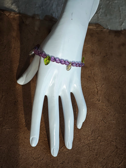 A purple hand-strung bracelet with luminous Czech glass beads & delicate botanical charms.
