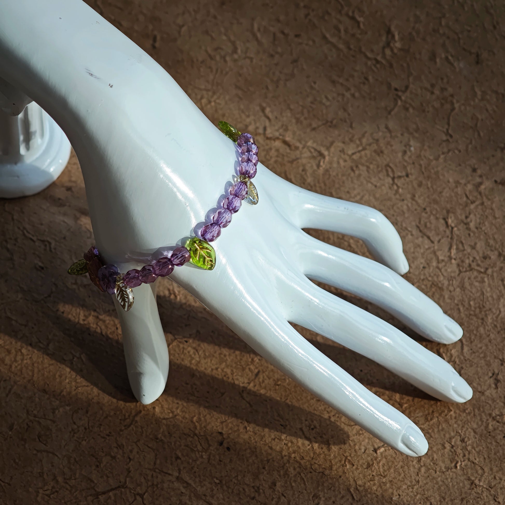 A purple hand-strung bracelet with luminous Czech glass beads & delicate botanical charms.