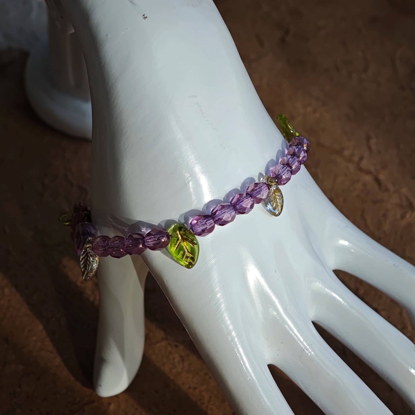 A purple hand-strung bracelet with luminous Czech glass beads & delicate botanical charms.