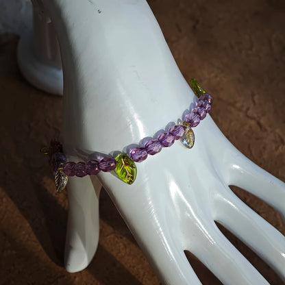 A purple hand-strung bracelet with luminous Czech glass beads & delicate botanical charms.