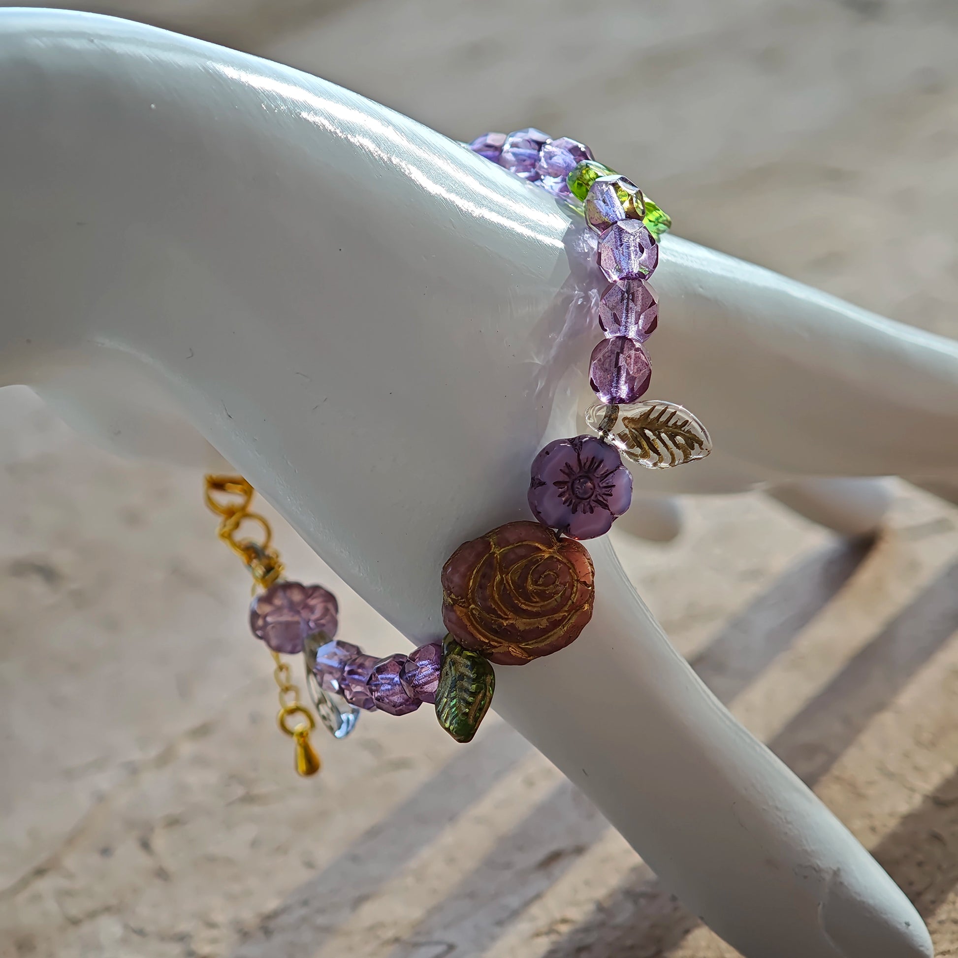 A purple hand-strung bracelet with luminous Czech glass beads & delicate botanical charms.