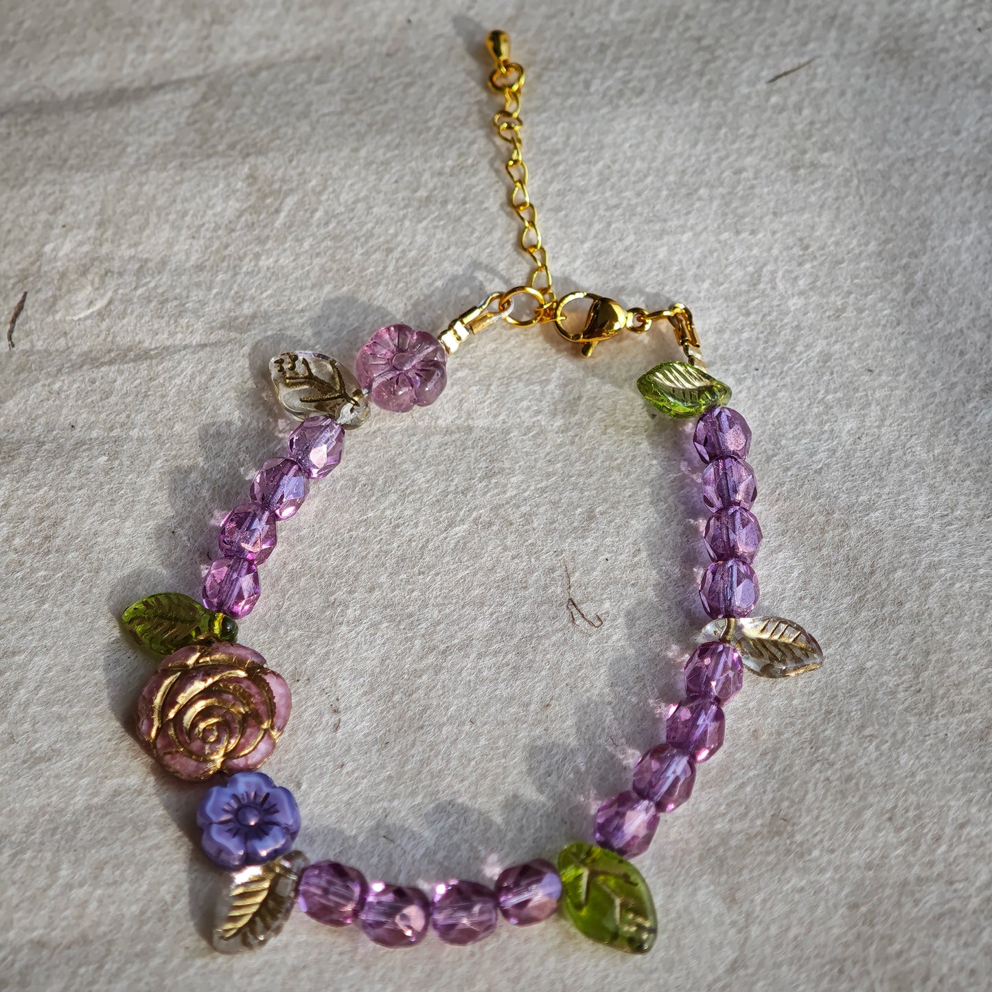 A purple hand-strung bracelet with luminous Czech glass beads & delicate botanical charms.