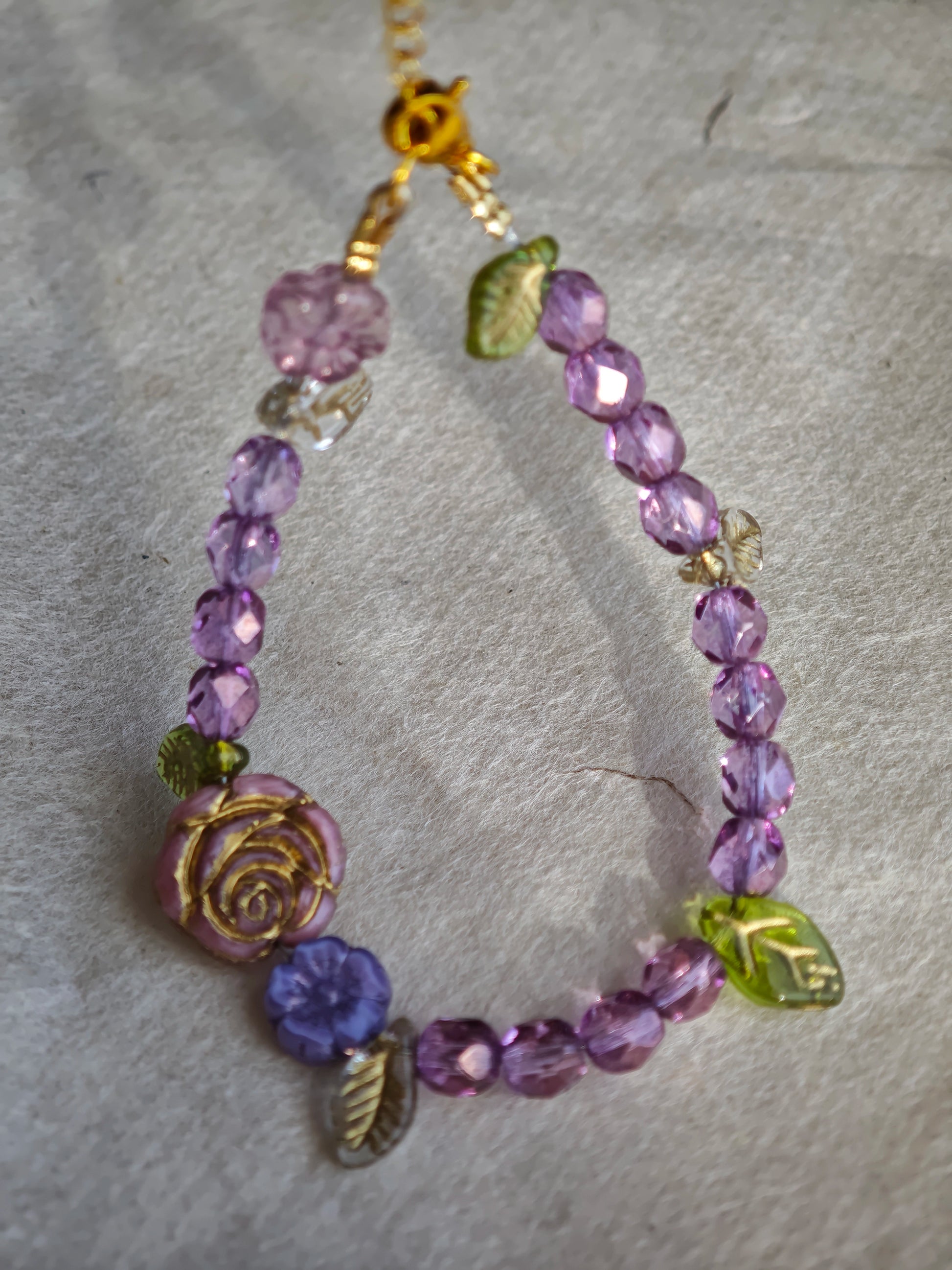 A purple hand-strung bracelet with luminous Czech glass beads & delicate botanical charms.