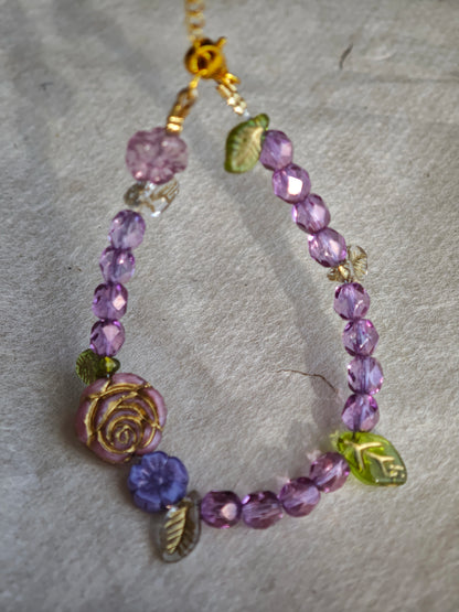 A purple hand-strung bracelet with luminous Czech glass beads & delicate botanical charms.