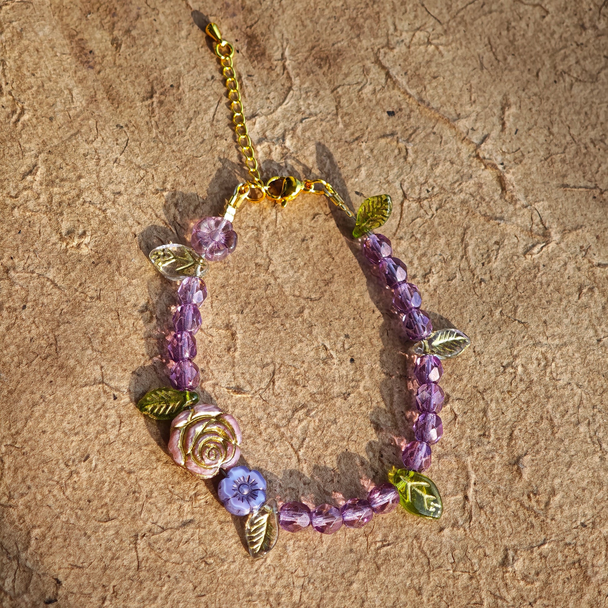 A purple hand-strung bracelet with luminous Czech glass beads & delicate botanical charms.