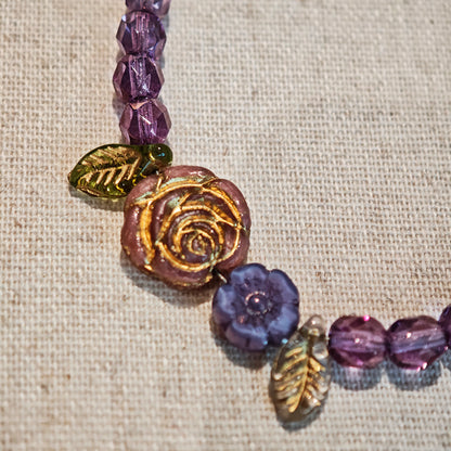 A purple hand-strung bracelet with luminous Czech glass beads & delicate botanical charms.