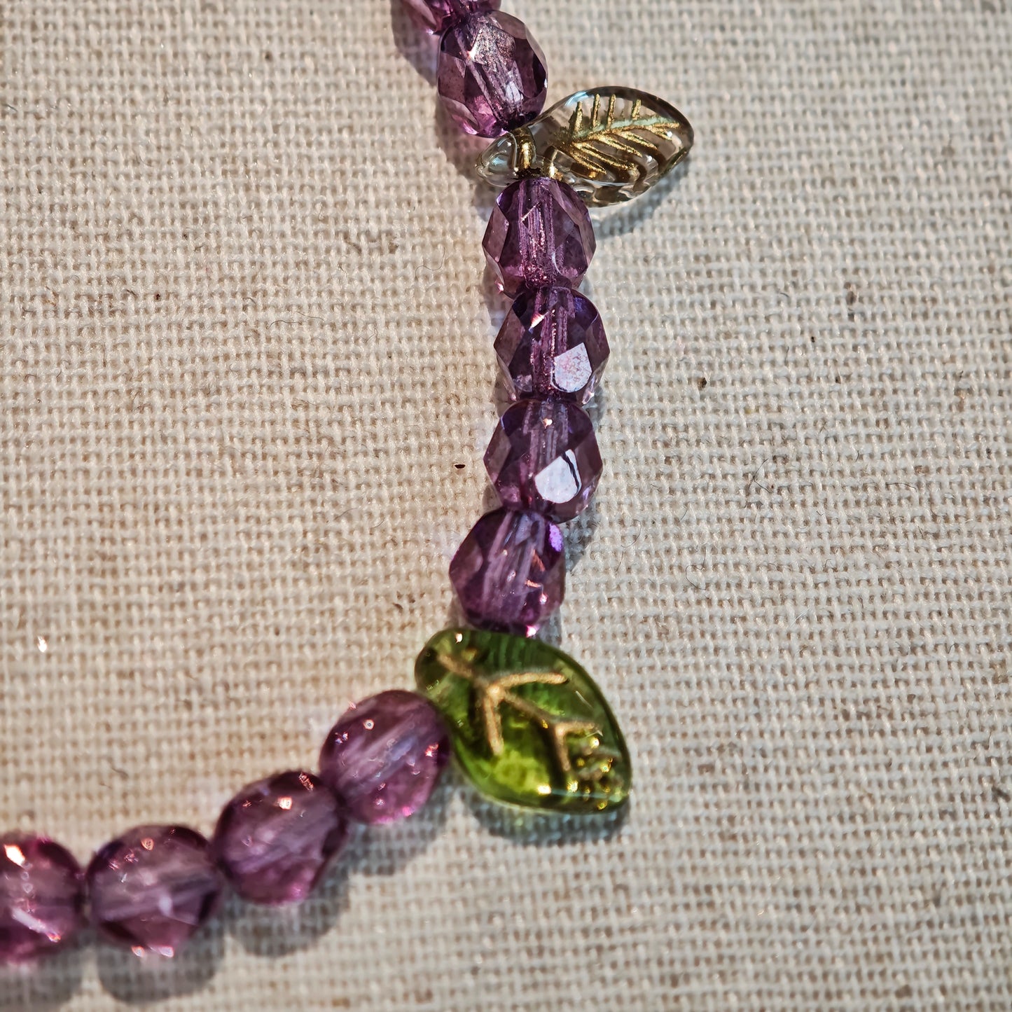 A purple hand-strung bracelet with luminous Czech glass beads & delicate botanical charms.
