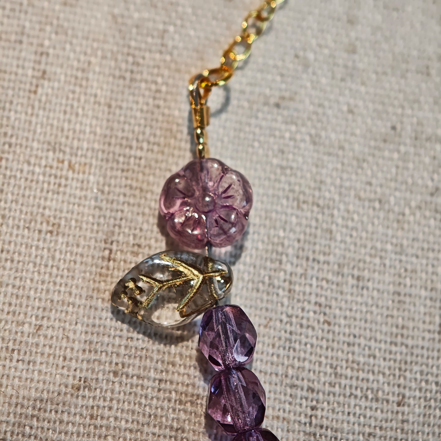 A purple hand-strung bracelet with luminous Czech glass beads & delicate botanical charms.