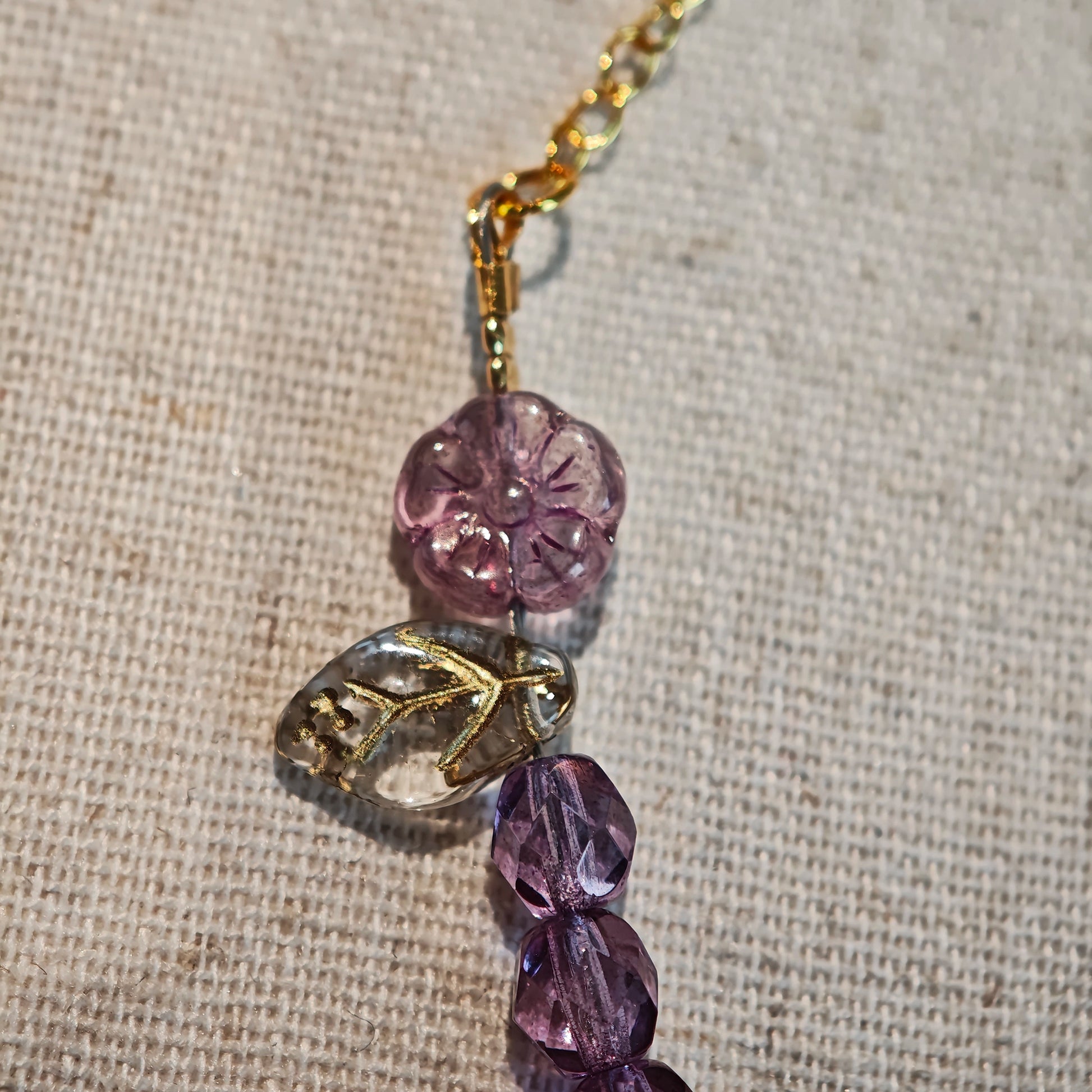 A purple hand-strung bracelet with luminous Czech glass beads & delicate botanical charms.
