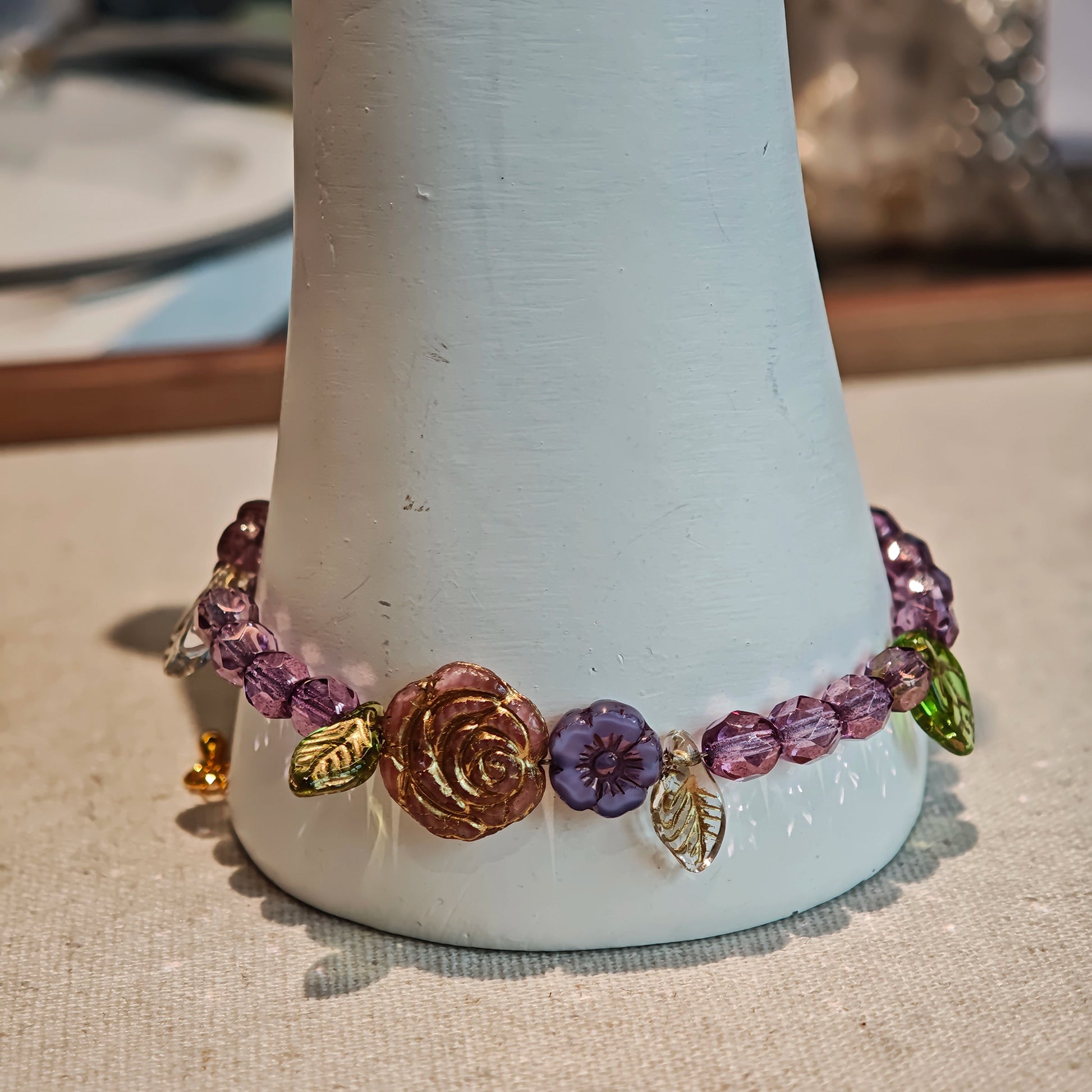 A purple hand-strung bracelet with luminous Czech glass beads & delicate botanical charms.