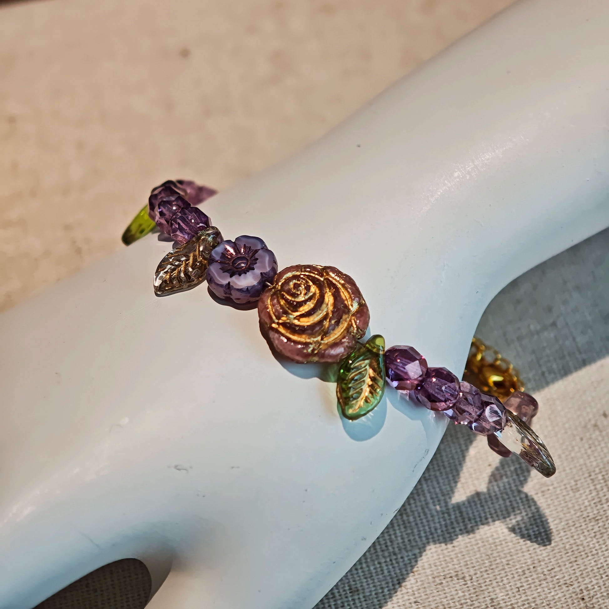 A purple hand-strung bracelet with luminous Czech glass beads & delicate botanical charms.