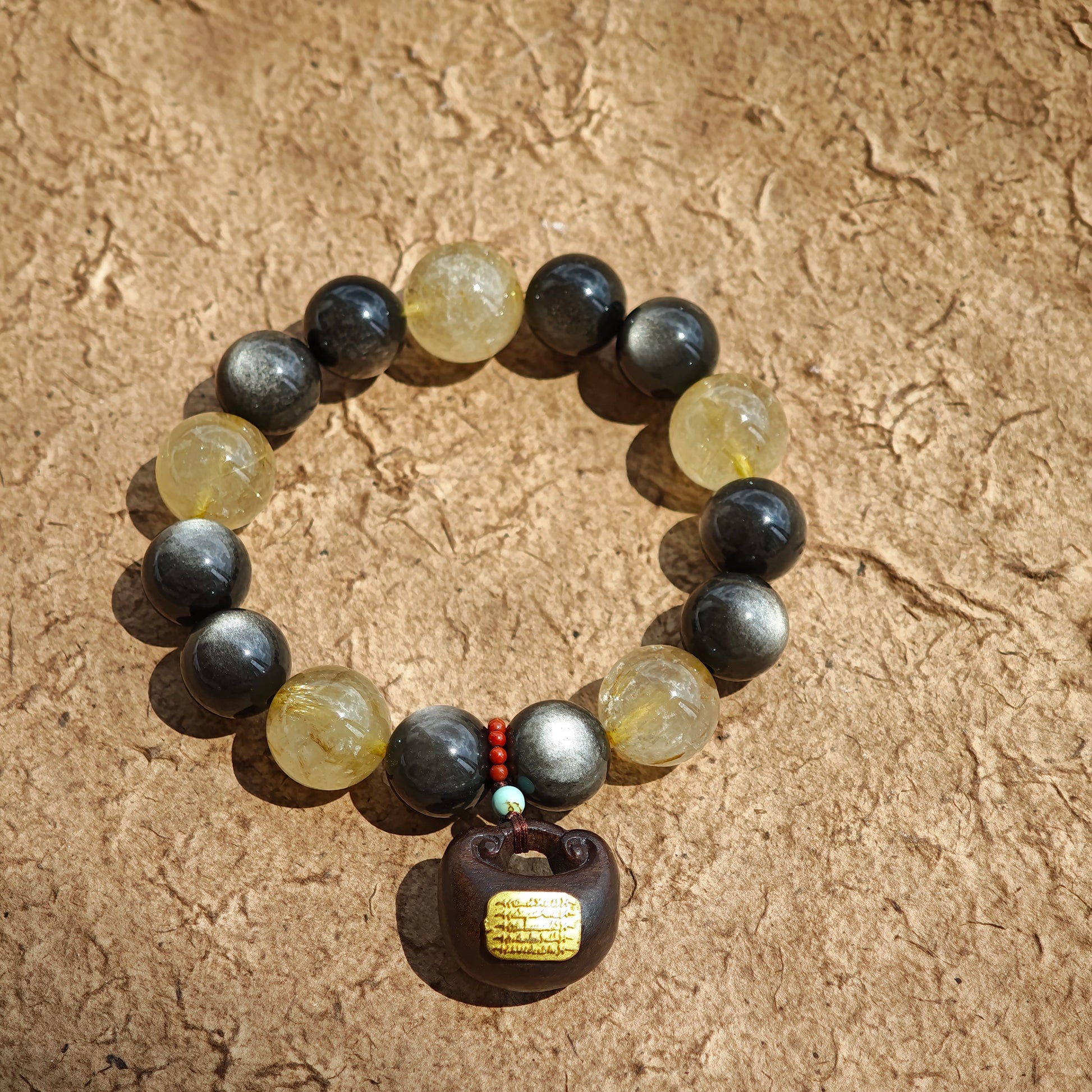 This is a silver sheen obsidian and rutilated quartz bracelet, finished with aloeswood and south red agate pendant—luxury forged in primal power.