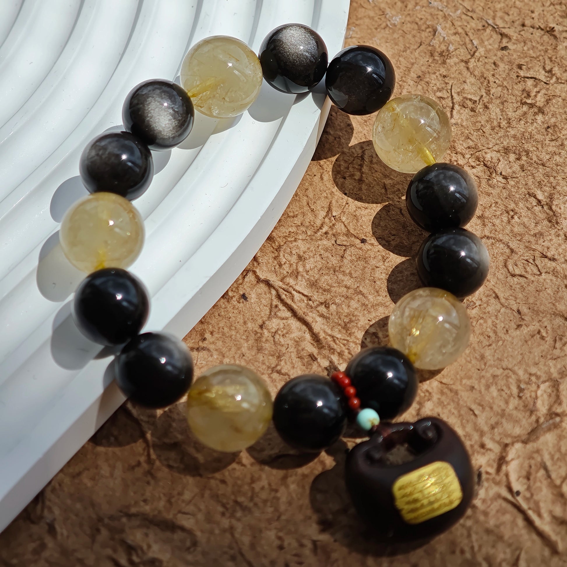 This is a silver sheen obsidian and rutilated quartz bracelet, finished with aloeswood and south red agate pendant—luxury forged in primal power.