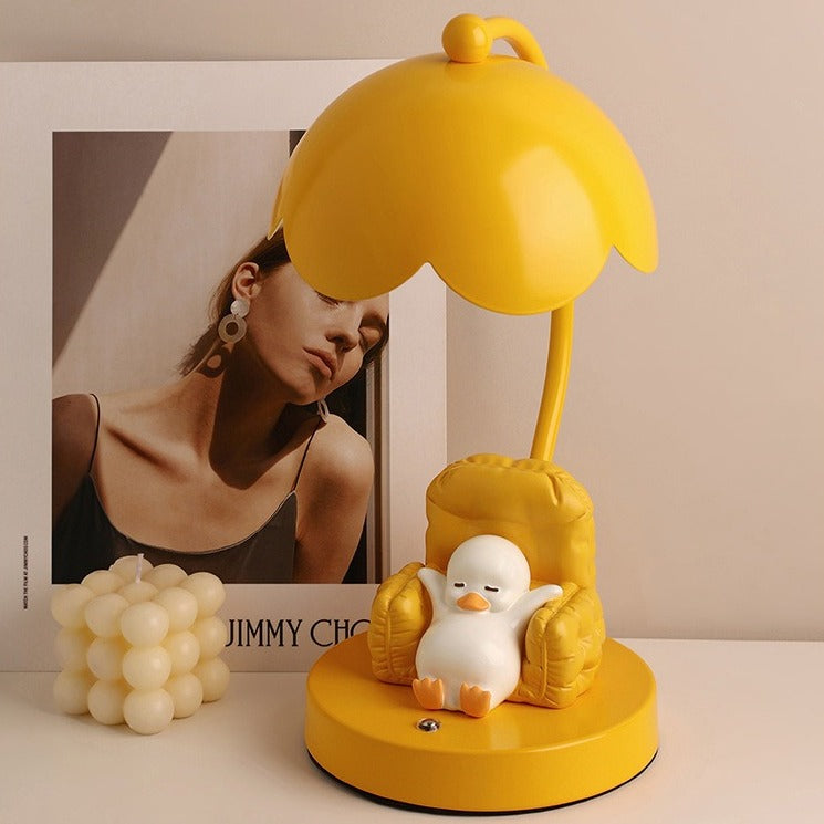 This is a bedside lamp with a design of a duck lying in a yellow sofa. And it comes with a round lampshade. Smooth rounded lines and artistic detailing make it a decorative bedside lamp and a comforting companion after long workdays.