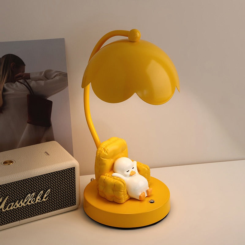 This is a bedside lamp with a design of a duck lying in a yellow sofa. And it comes with a round lampshade. Smooth rounded lines and artistic detailing make it a decorative bedside lamp and a comforting companion after long workdays.