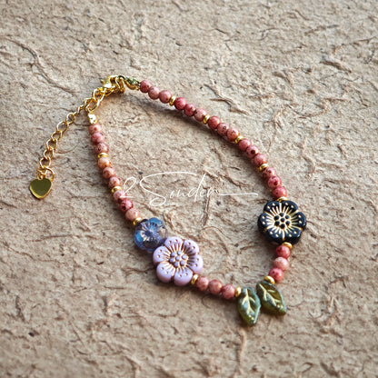 This is a bracelet that made of Czech beads. And it's highlighted by blue, purple, and black flower charms and green leaf accents, creating a stunningly attractive design.